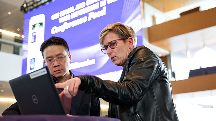 A man and woman talk in front of a laptop while the woman points at the screen