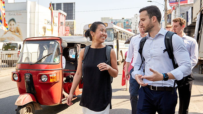 Smiling students walk down the street as a red rickshaw drives by