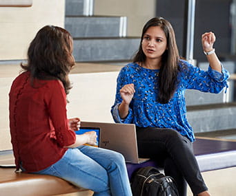 Two women talk next to a laptop